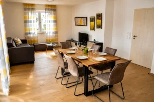 Modernes Wohn- und Esszimmer mit gedecktem Holztisch, grauem Sofa und hellen Vorhängen