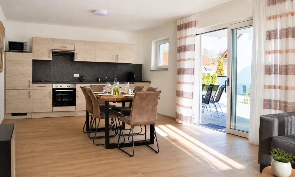 Wohnesszimmer & Küche - Tisch mit voll ausgestatteter Küche im Hintergrund - Terrasse mit Gartenmöbeln