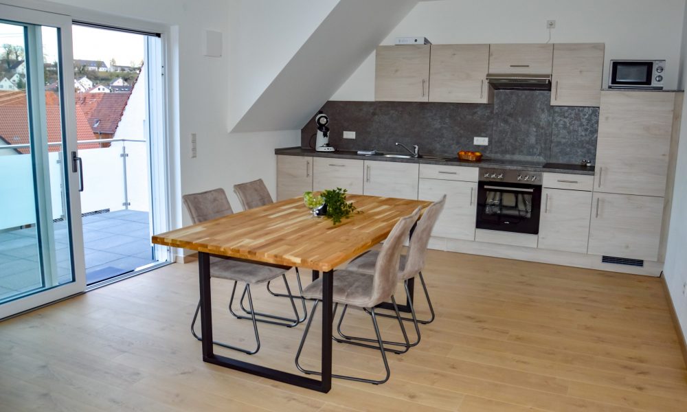 Wohnesszimmer & Küche - Tisch mit voll ausgestatteter Küche im Hintergrund