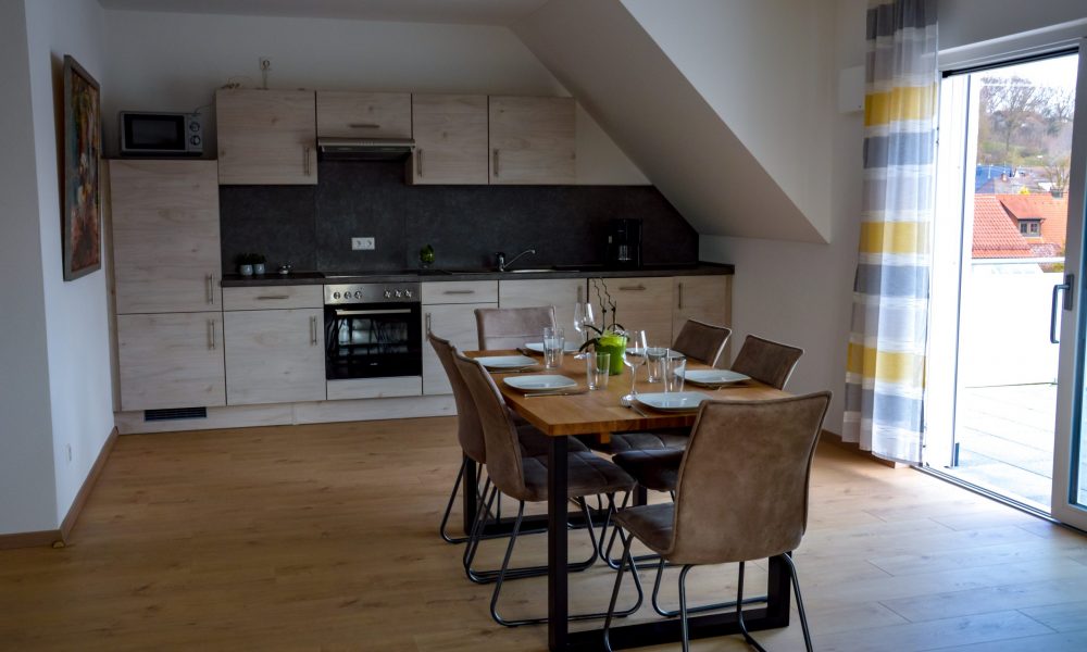 Wohnesszimmer & Küche - Tisch mit voll ausgestatteter Küche im Hintergrund